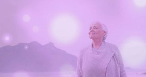 Senior woman gazing toward horizon on pastel shore, serene contemplative elder portrait