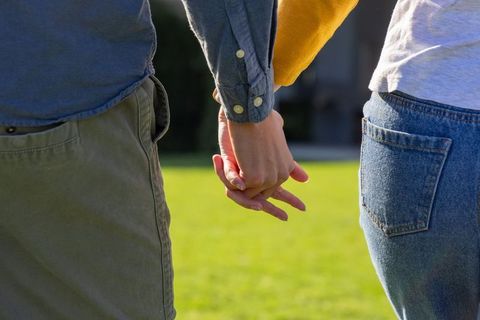Couple holding hands interlaced behind hips on sunlit green lawn