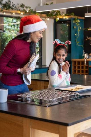 Asian mother and daughter baking holiday cookies in festive kitchen wearing santa hats