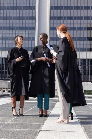 Diverse female graduates celebrating on urban rooftop holding diplomas and gowns