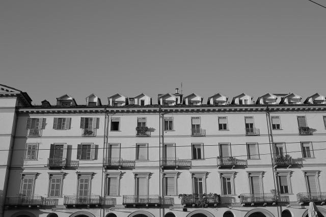 View of a historic European building showcasing symmetrical architecture and repeating windows and balconies. Black and white photography enhances the timeless quality of the design. Ideal for use in materials related to architecture, history, urban studies, and travel.