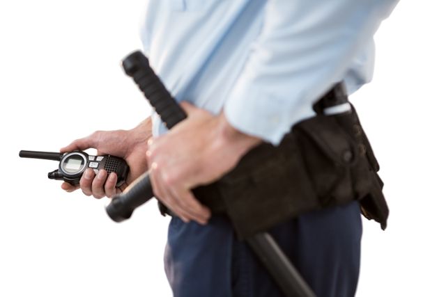 Security officer holding a walkie-talkie and baton, dressed in uniform. Ideal for use in articles, advertisements, or websites related to security services, law enforcement, public safety, and professional security equipment.