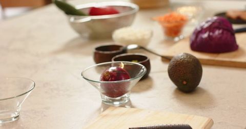 Red onion sitting in clear glass bowl on stone countertop with avocado and purple cabbage