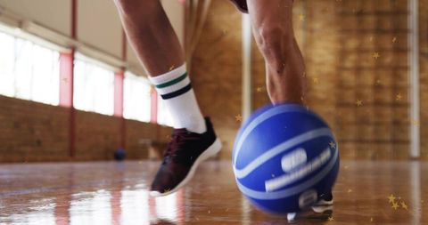 Male athlete dribbling blue basketball on indoor hardwood court with striped socks