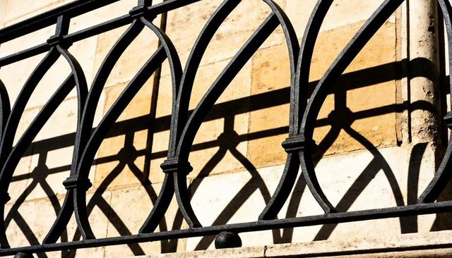 Ornate wrought iron railing casting arched geometric shadows on warm stone facade