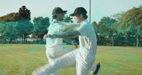 Cricket teammates hugging and celebrating victory in white uniforms on sunlit grass field