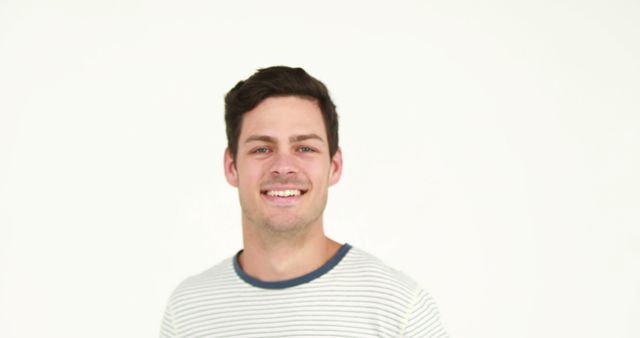 Young man with dark hair wearing a casual striped t-shirt, smiling. Plain white background conveys simplicity. Ideal for use in advertising, corporate websites, profiles, or any content that calls for a friendly, approachable look.