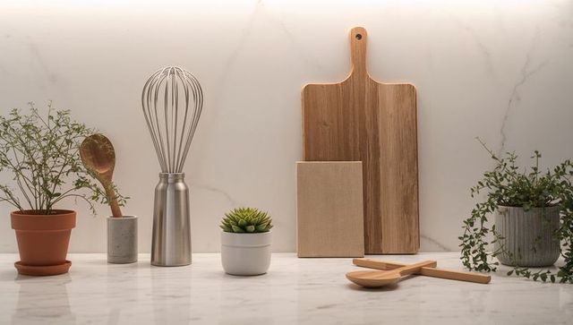 Minimalist kitchen vignette featuring wooden cutting boards, whisk, plants on marble