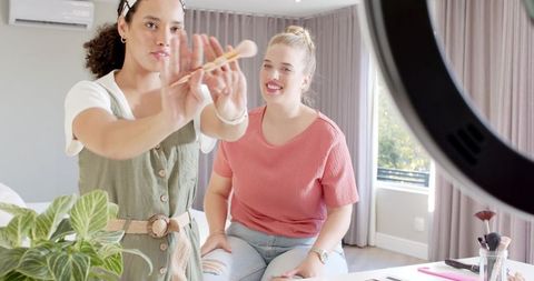 Female friends filming makeup tutorial at home with ring light