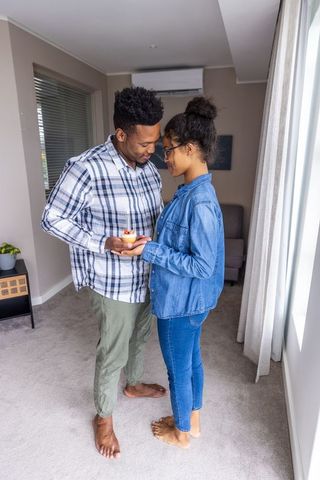 Barefoot couple sharing intimate moment holding cupcake with lit candle at home