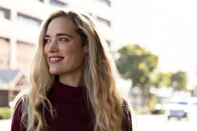 Young woman smiling and looking left wearing maroon turtleneck on sunny city street