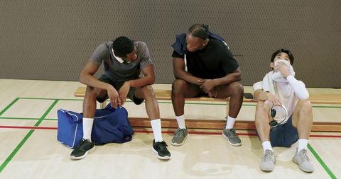 Diverse male teammates resting on bench sharing headphones and conversation after workout