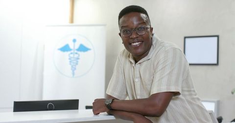 Smiling african man leaning on clinic reception desk welcoming patients