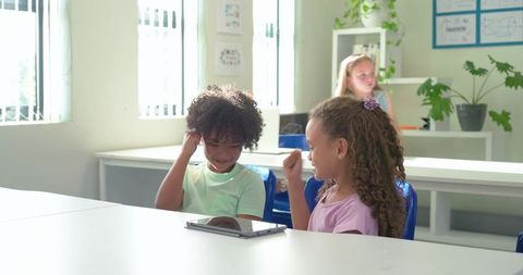 Elementary Students Using Tablet in Bright Classroom Collaborating and Celebrating Success