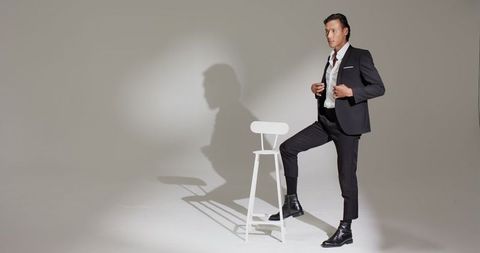 Elegant man posing in black suit against minimalistic background