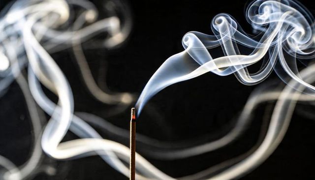 Incense stick burning graceful curling smoke plumes over dark background minimalist macro