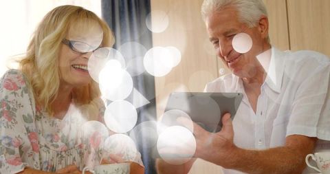 Senior couple sharing tablet and tea, smiling together in cozy kitchen nook