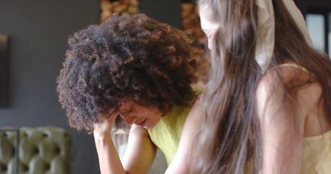 Comforting friend offering emotional support to woman holding head on living room sofa