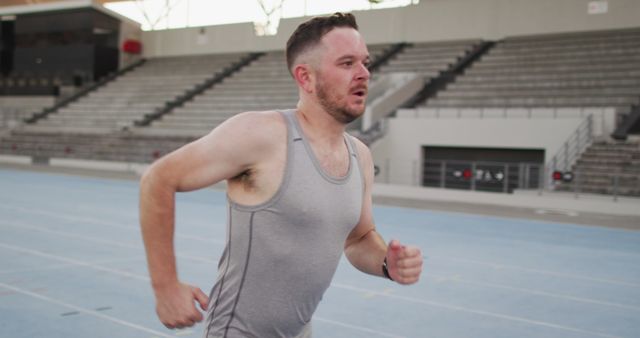 Man in gray sportswear running on a track in an empty stadium during daytime. Ideal for use in content related to fitness, active lifestyle, athletic training, outdoor workouts, motivational fitness blogs, and health and wellness advertisements.