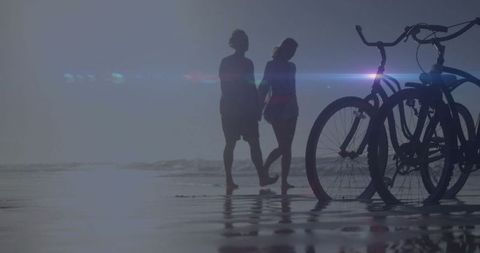 Couple walking hand in hand on beach with bicycles