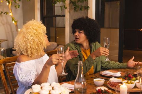 Couple sharing animated conversation and clinking champagne flutes at cozy dinner party