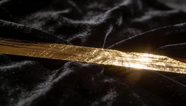 Gilded light on black velvet ribbon creating luxurious gold sheen and dramatic contrast