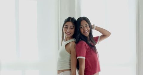 Diverse female friends smiling back to back in modern minimalist room