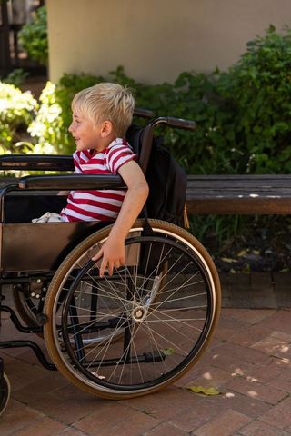 Smiling child in wheelchair enjoying sunny courtyard with backpack on bench