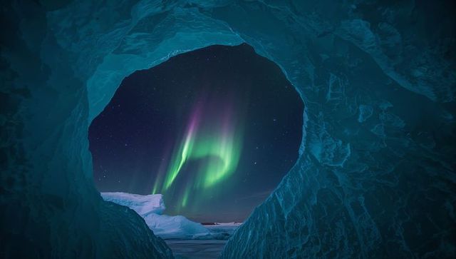Turquoise ice grotto framing aurora borealis over iceberg and pack ice nightscape