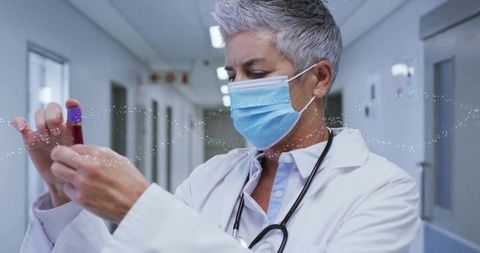 Physician Inspecting Blood Vial in Hospital Corridor Wearing Surgical Mask and Stethoscope