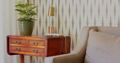 Cozy living room nook with wooden side table, green planter, brass lamp and patterned wallpaper