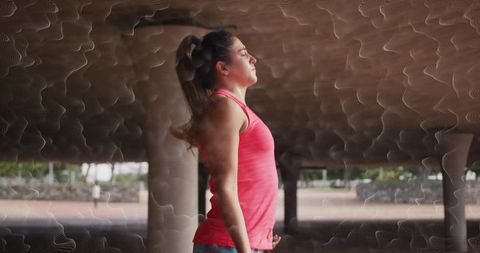 Female athlete taking deep breath while stretching beneath shelter columns