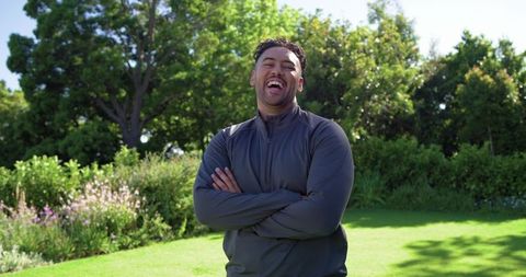 African american man laughing with arms crossed on sunny lawn casual outdoor portrait