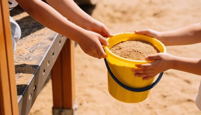 Passing yellow sand bucket between children at playground during sunny playtime
