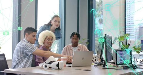 Diverse team collaborating over laptop with VR headsets in modern open-plan office