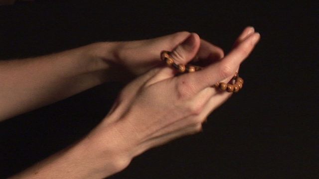 Hands held in prayer gently clasping a rosary, wood beads suggesting approachability and warmth. The dark background emphasizes a solitary moment of devotion and spiritual focus. Ideal for use in religious publications, marketing for religious organizations, illustrating meditation guides or articles about prayer, and any materials promoting peace and reflection.