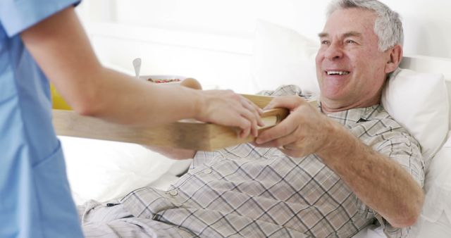 Elderly man lying in a hospital bed receiving a meal from a nurse. The setting depicts a care environment with an emphasis on patient care. Use this for illustrating healthcare services, medical assistance, elderly care and support, and hospital recovery process.