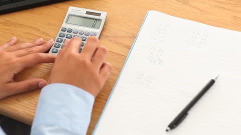Hands Calculating with a Calculator and Notebook in Office