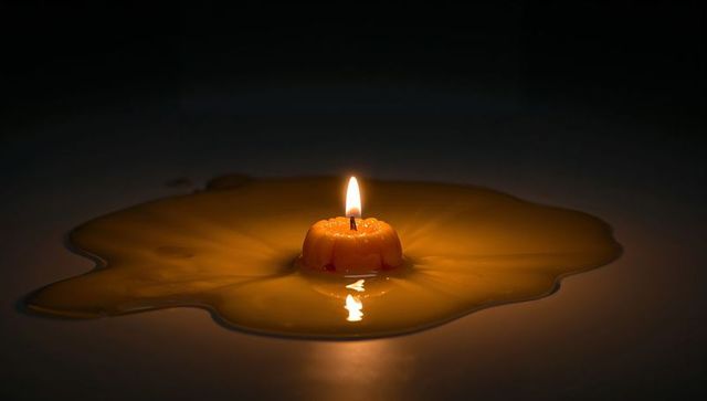 Candle Flame Illuminating Pool of Melted Wax on Reflective Surface