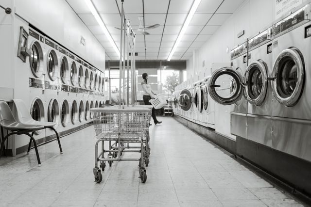 Empty Laundromat with Washing Machines and Cart, Person in Background - Download Free Stock Photos Pikwizard.com