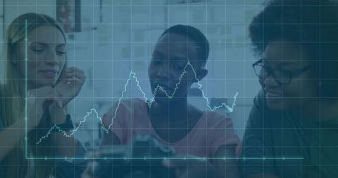 Collaborating women analyzing mobile data with financial graph overlay in modern workspace
