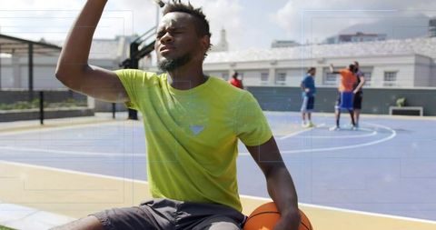 Cooling down on rooftop basketball court holding ball in neon shirt under bright urban sun