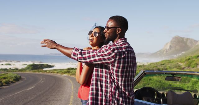 African american couple embracing each other while standing near convertible car on road. road trip travel and adventure concept