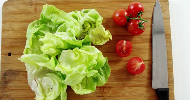 Image shows fresh lettuce and tomatoes placed on a wooden cutting board with a knife beside. Useful for recipes, cooking blogs, healthy eating articles, vegan diet promotion, or kitchen product advertisements.
