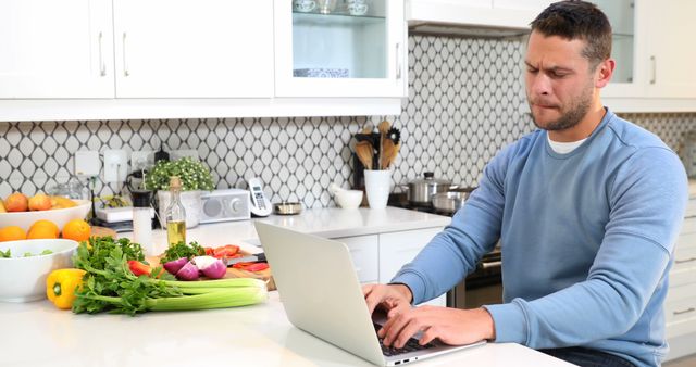 Man working on laptop in kitchen while preparing vegetables - Download Free Stock Images Pikwizard.com