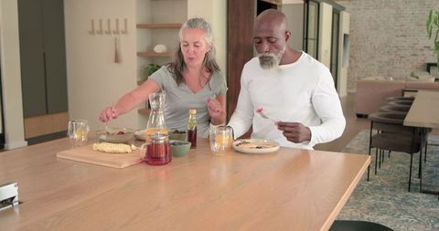Mature interracial couple sharing relaxed breakfast at modern kitchen island, cozy dining