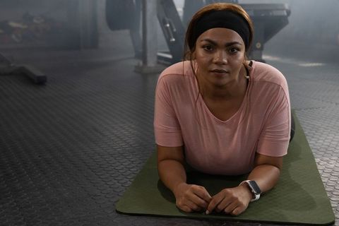 African american woman holding forearm plank on green mat in gym, showing core strength