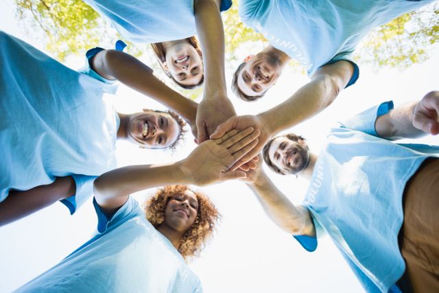 Diverse group of volunteers forming a huddle in a park, symbolizing teamwork and unity. Ideal for use in campaigns promoting community service, charity events, social work, and team-building activities. Perfect for illustrating concepts of collaboration, support, and positive group dynamics.