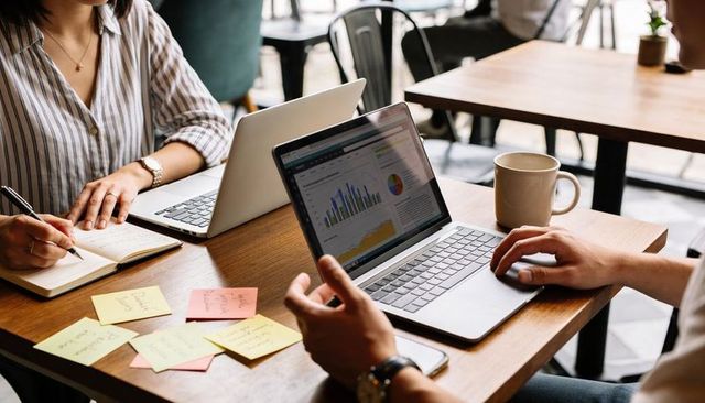 Young professionals collaborating over laptops and sticky notes in casual cafe workspace