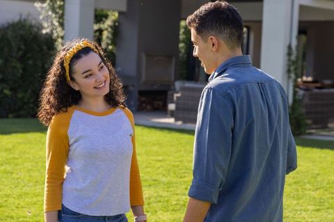 Young couple chatting and smiling on backyard lawn beside covered patio on sunny day